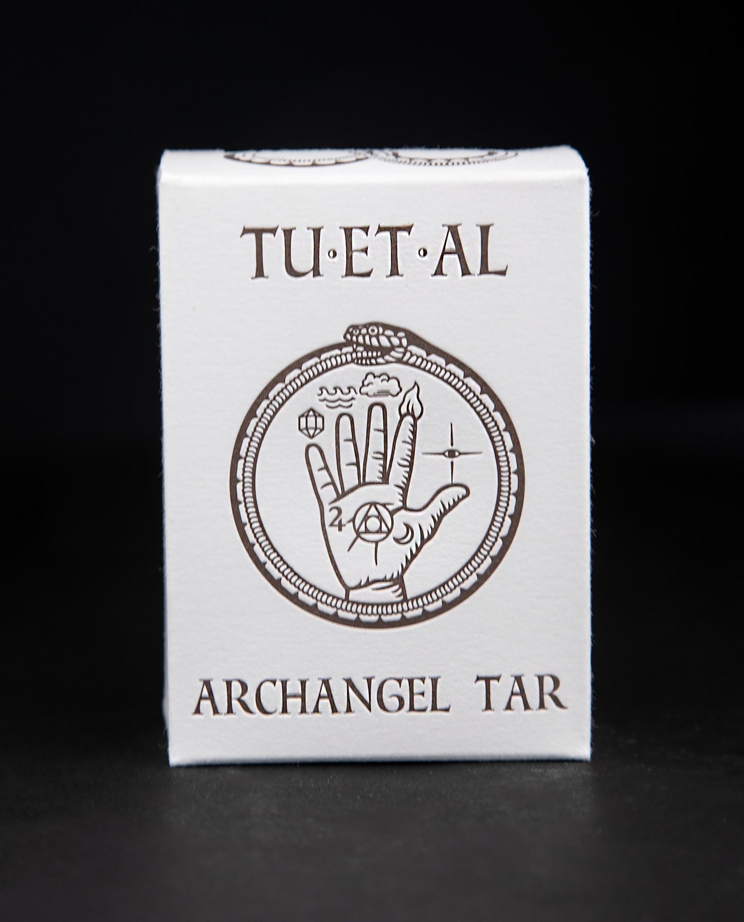 Box of TU-ET-AL's "archangel tar" soap against a black background. The box features an illustration of a snake eating its own tail and an alchemical hand in dark brown