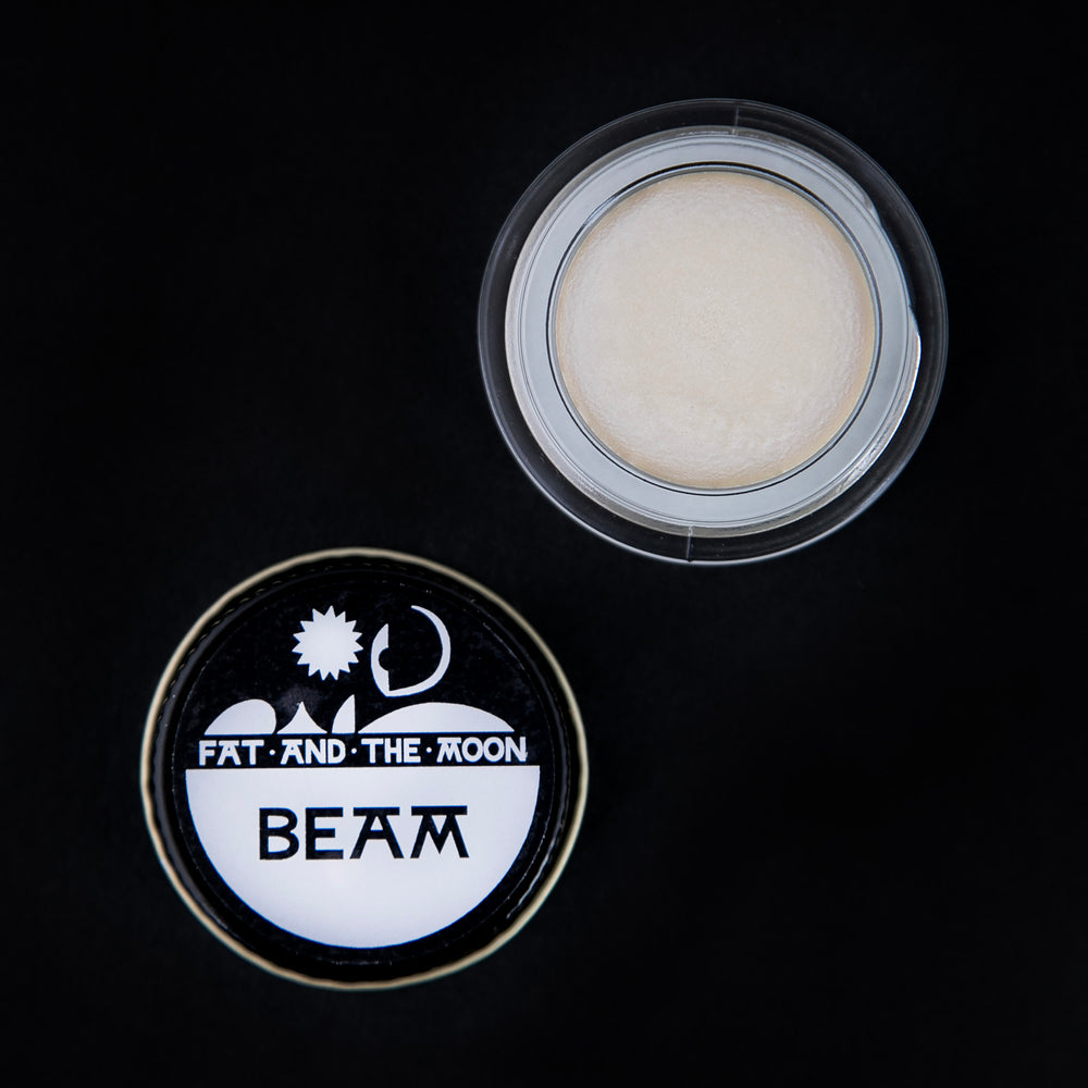 open glass pot of Fat and the Moon's "Beam" highlighter, revealing a shimmery white makeup product