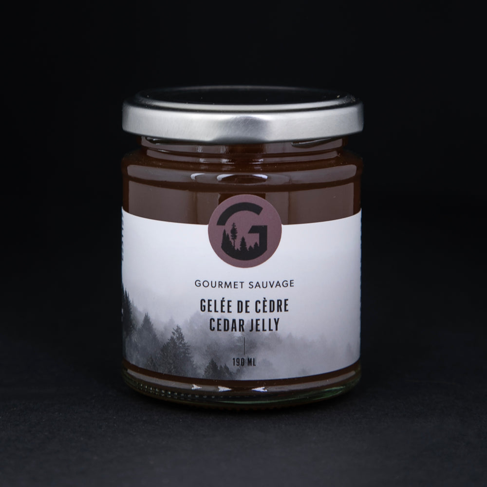 Clear glass jar with metal lid of Gourmet Sauvage's cedar jelly, sitting on black background