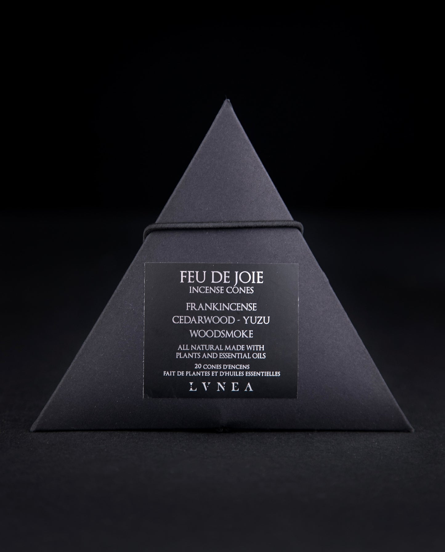 A closed black paper pyramid box of LVNEA's 'Feu de Joie' incense. The black label on the box reads "Feu de Joie Incense Cones: Frankincense, Cedarwood, Yuzu, Woodsmoke" in silver foil