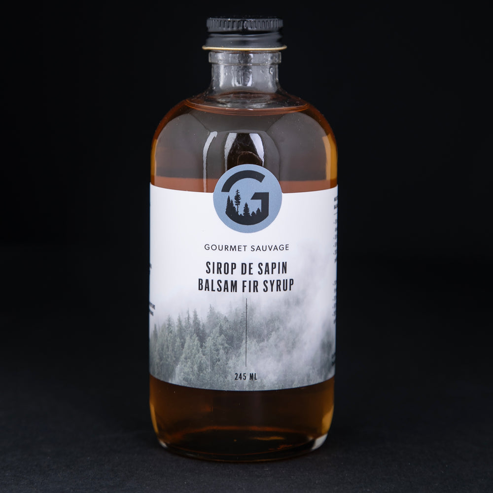 Clear bottle of Gourmet Sauvage's balsam fir syrup, sitting on black background