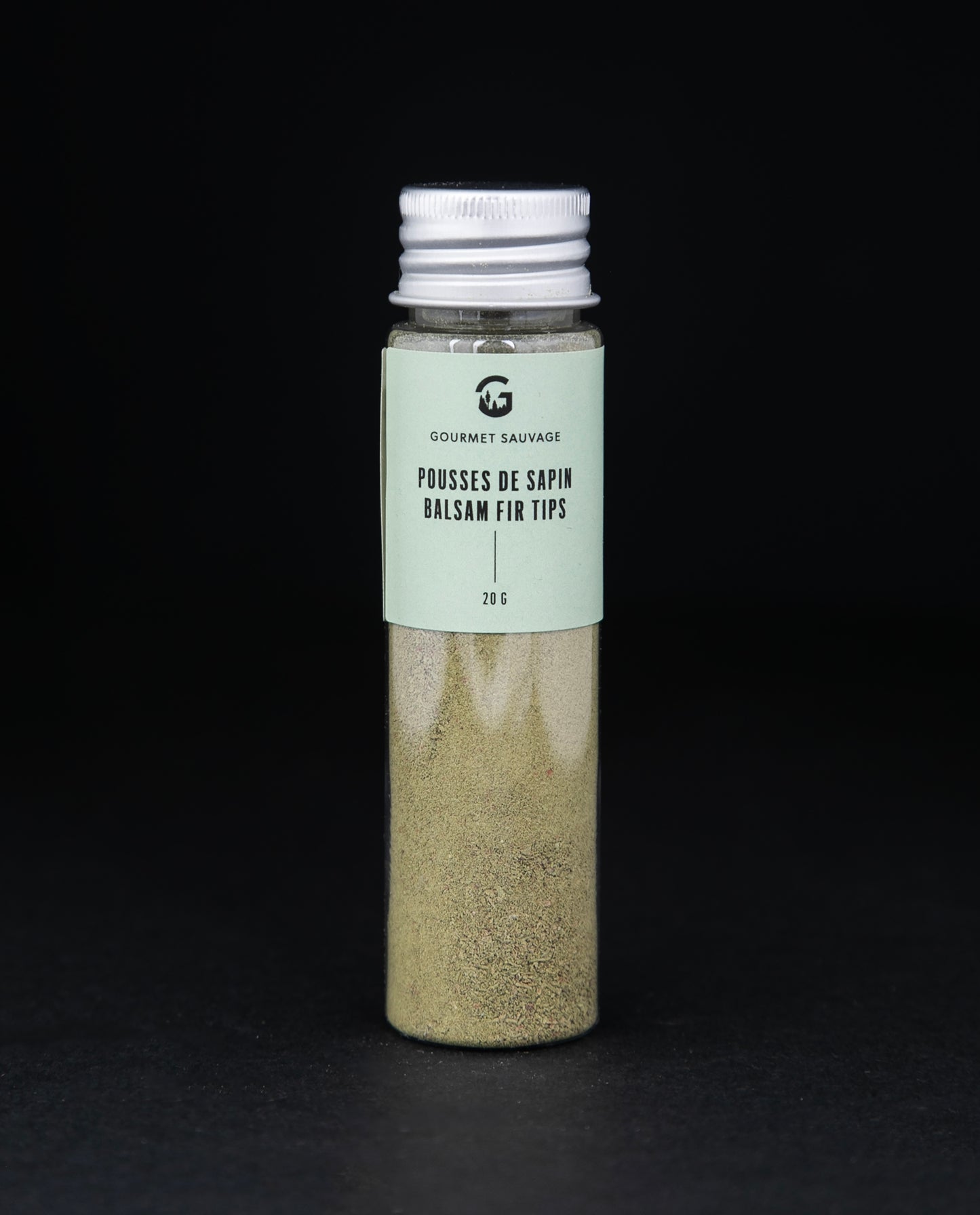 Clear tube of Gourmet Sauvage's balsam fir tip powder, sitting on black background. The powder is a vibrant green colour.