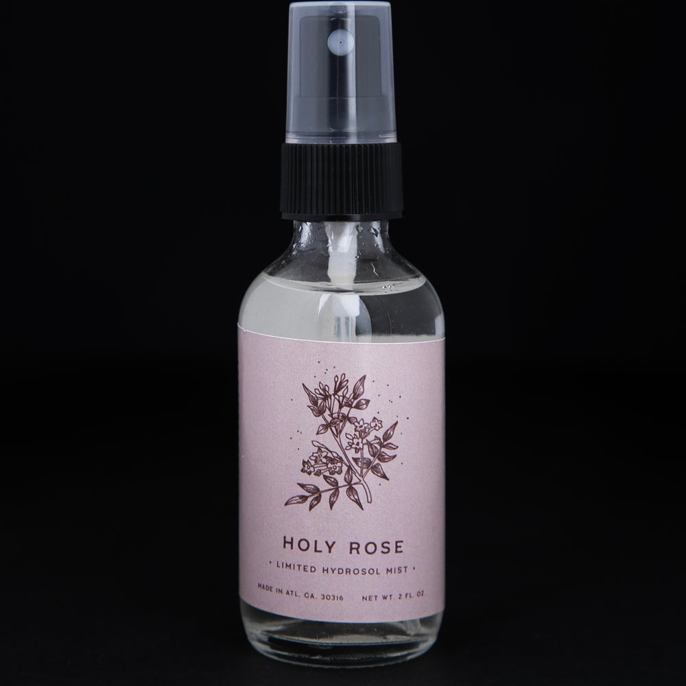 2oz clear glass bottle with black spray top of Rowan & Sage's "Holy Rose" hydrosol. The label on the bottle is light pink.