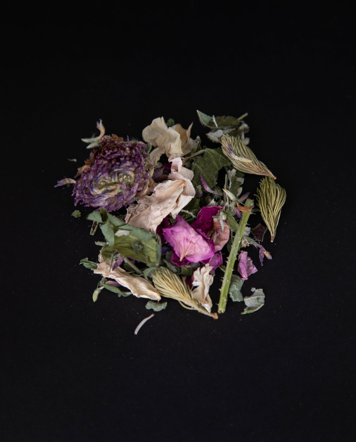 handful of loose "La Florale" tea on a black background. The herbal blend is colourful and includes rose petals, spruce tips, and and clover buds.