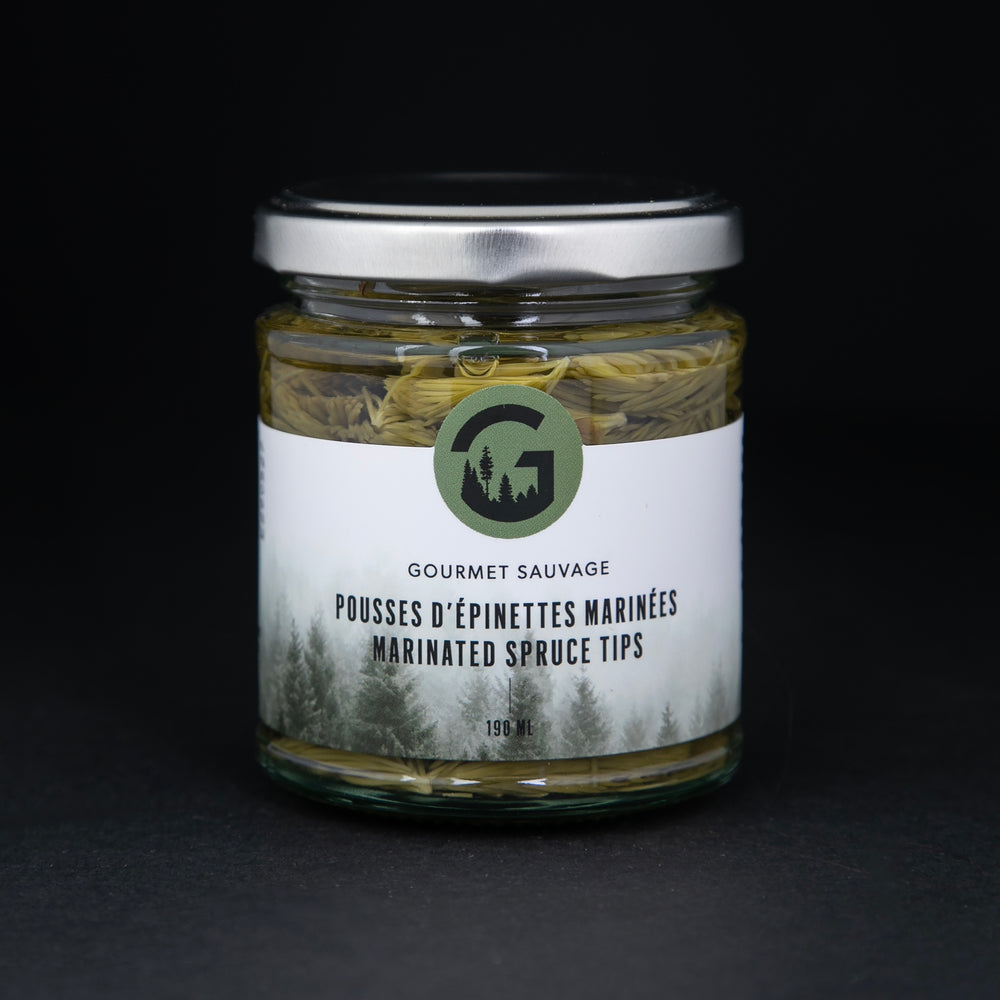 Clear glass jar with metal lid of Gourmet Sauvage's marinated spruce tips, sitting on black background