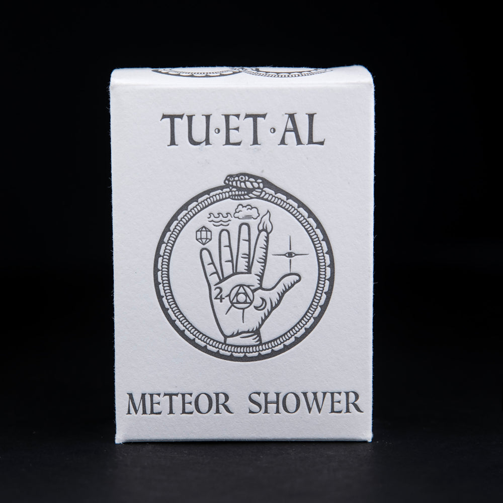 White cardboard soap box containing TU-ET-AL's "Meteor Shower" soap. There is an illustration of a snake eating it's own tail, and an alchemical hand on front in grey.