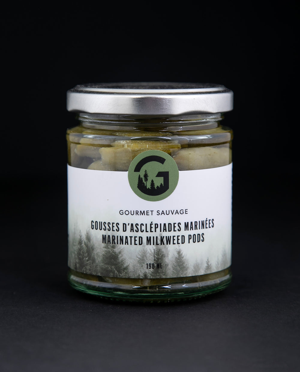 marinated milkweed pods in a glass jar against a black background