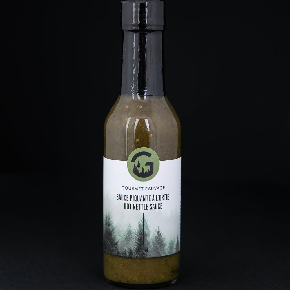 Clear glass bottle of Gourmet Sauvage's nettle hot sauce, sitting on black background