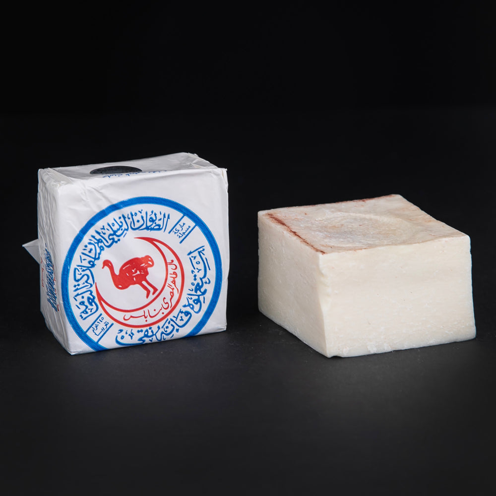 Wax paper-wrapped olive oil soap, sitting next to an unwrapped bar of soap on black background