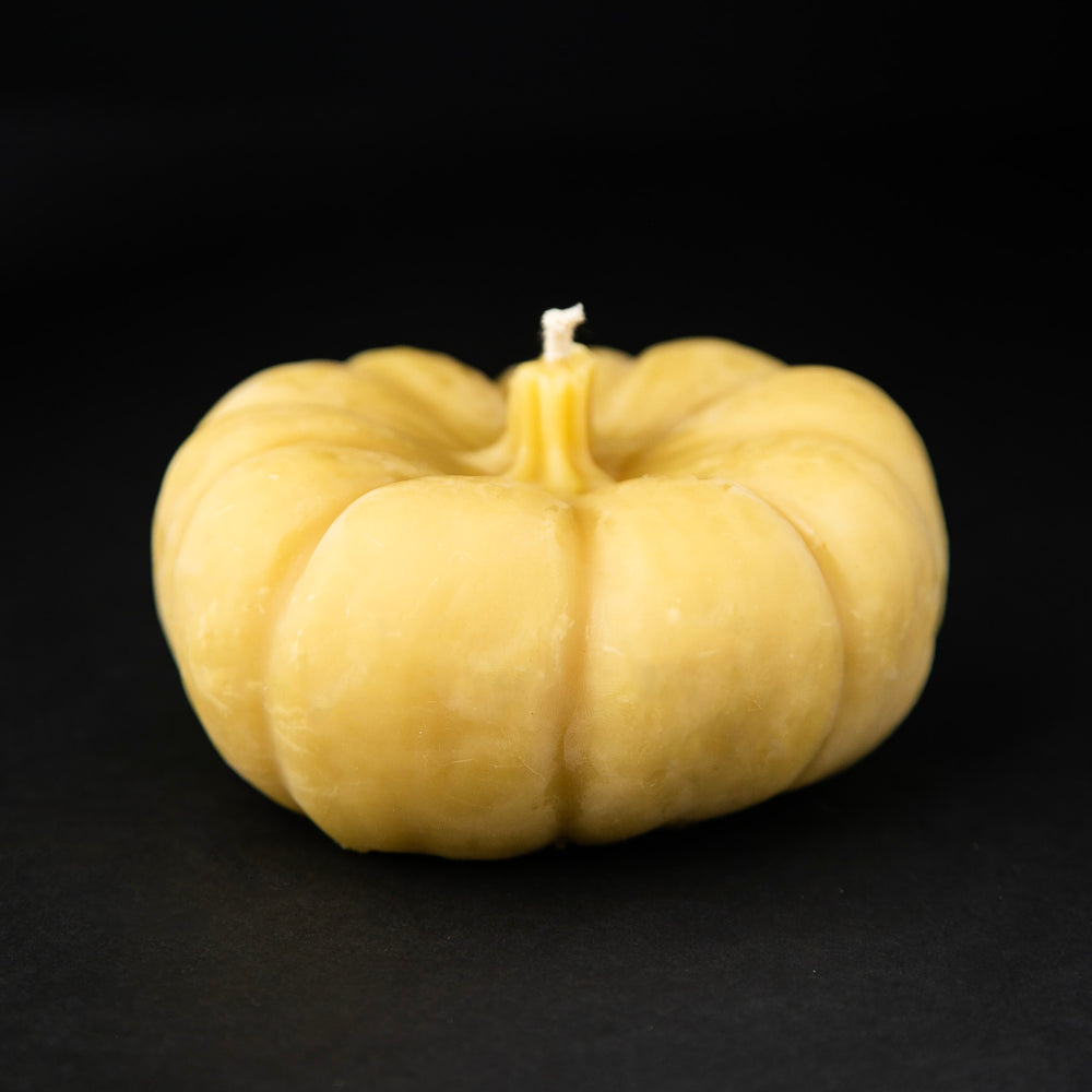 A golden pumpkin-shaped beeswax candle on black background.