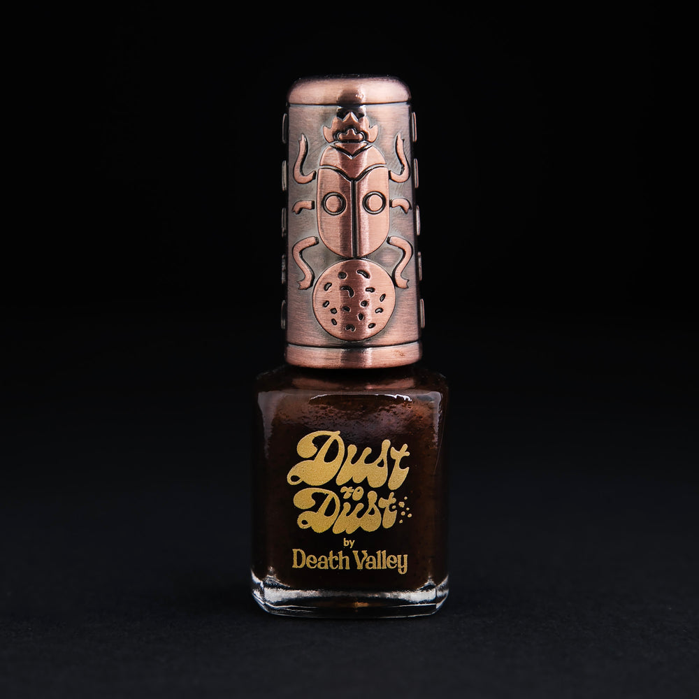 bottle of Death Valley Nail's "Reisi" polish, against a black background. The polish is dark brown, and the bottle has a decorative bronze cap.