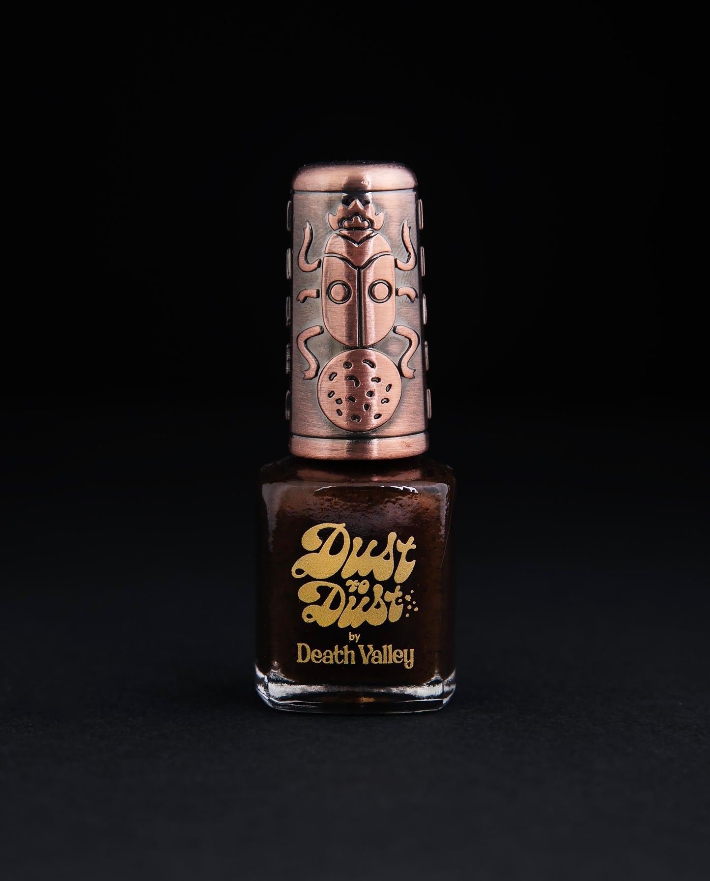 bottle of Death Valley Nail's "Reisi" polish, against a black background. The polish is dark brown, and the bottle has a decorative bronze cap.