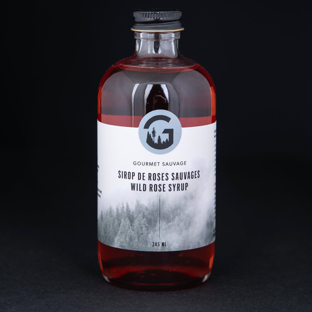 Clear bottle of Gourmet Sauvage's wild rose syrup, sitting on black background