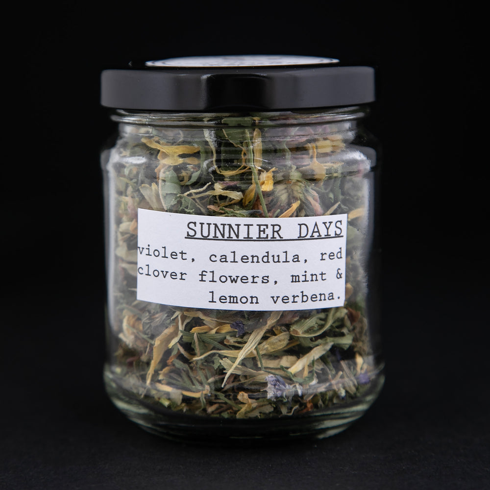 Clear glass jar of Bleuberryjams Sunnier Days herbal tea on black background