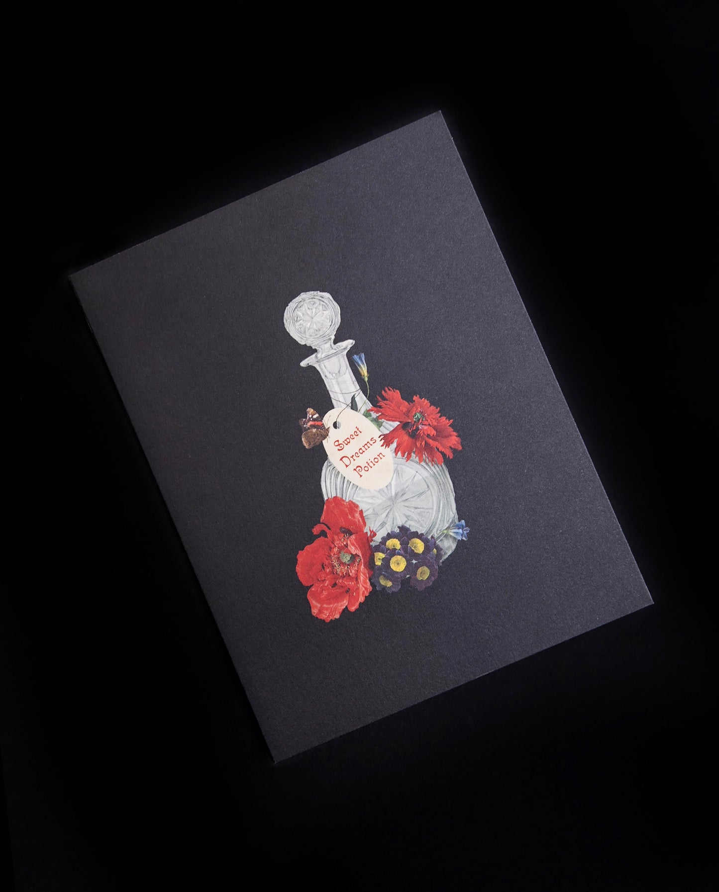 black greeting card with illustration of vintage glass bottle and red botanicals