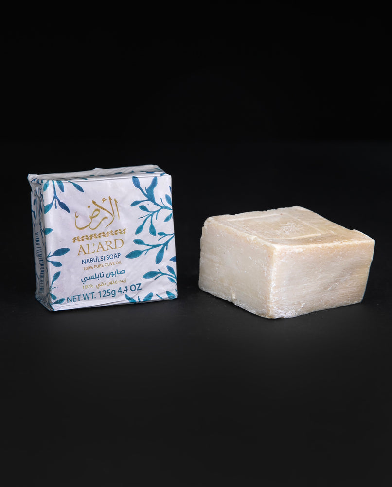 Wax paper-wrapped bar of olive oil soap next to unwrapped bar of soap. sitting on black background