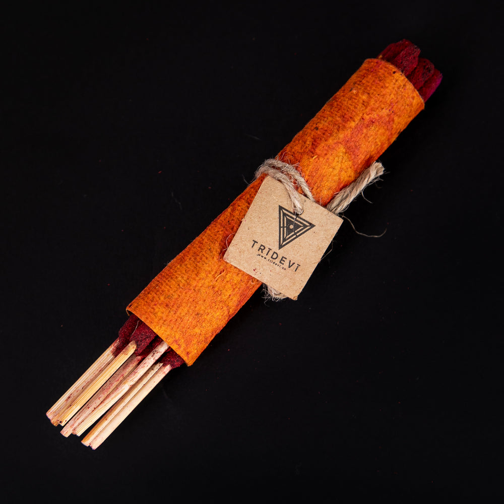 bundle of TriDevi 'Red Lotus' incense sticks wrapped in handmade orange paper, against a black background