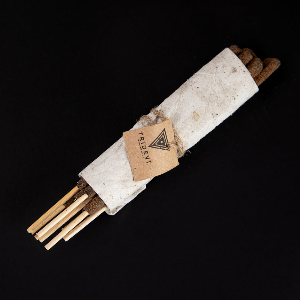 Bundle of sandalwood incense wrapped in handmade cream-coloured paper, sitting against a black background