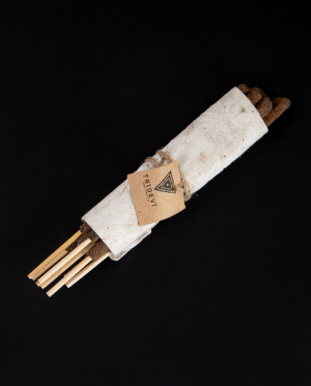 Bundle of sandalwood incense wrapped in handmade cream-coloured paper, sitting against a black background