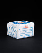 Side view of a bar of Palestinian olive oil soap, wrapped in white wax paper stamped with blue and red "Two Keys" logo