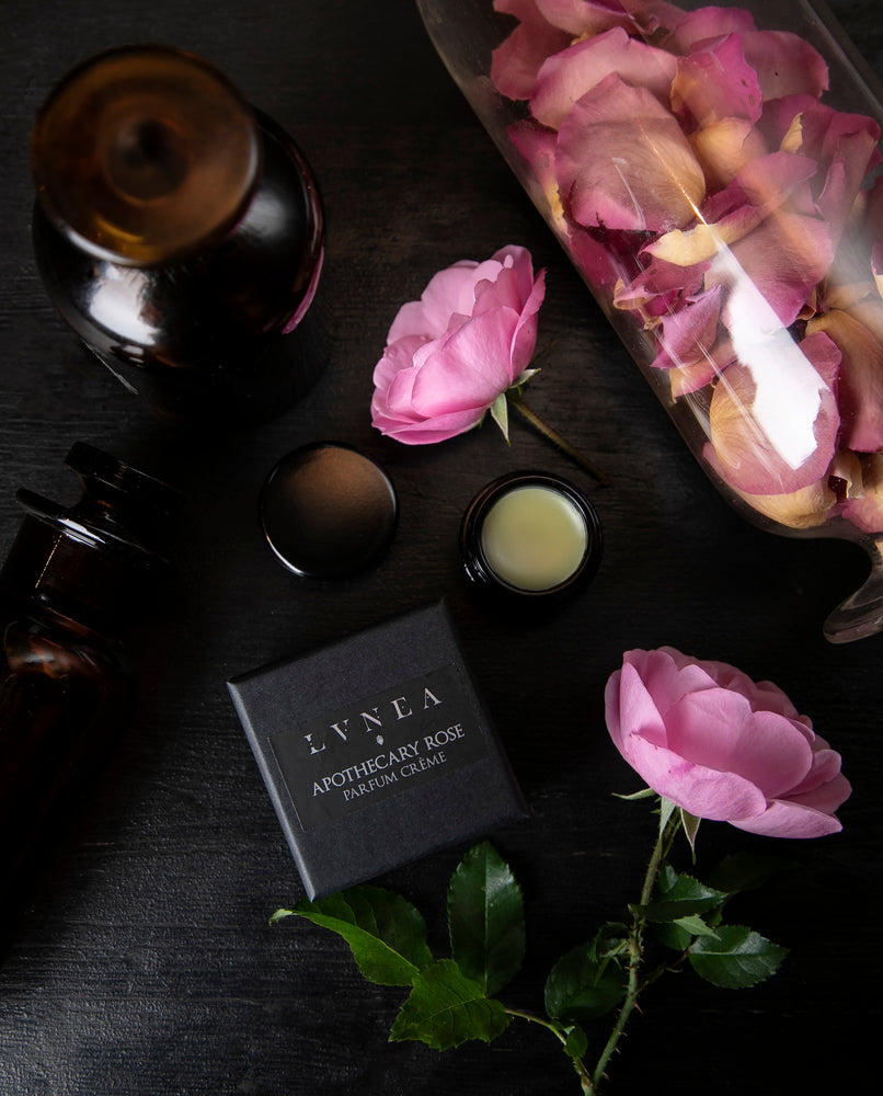 overhead view of opened jar of solid perfume next to fresh roses and apothecary jars