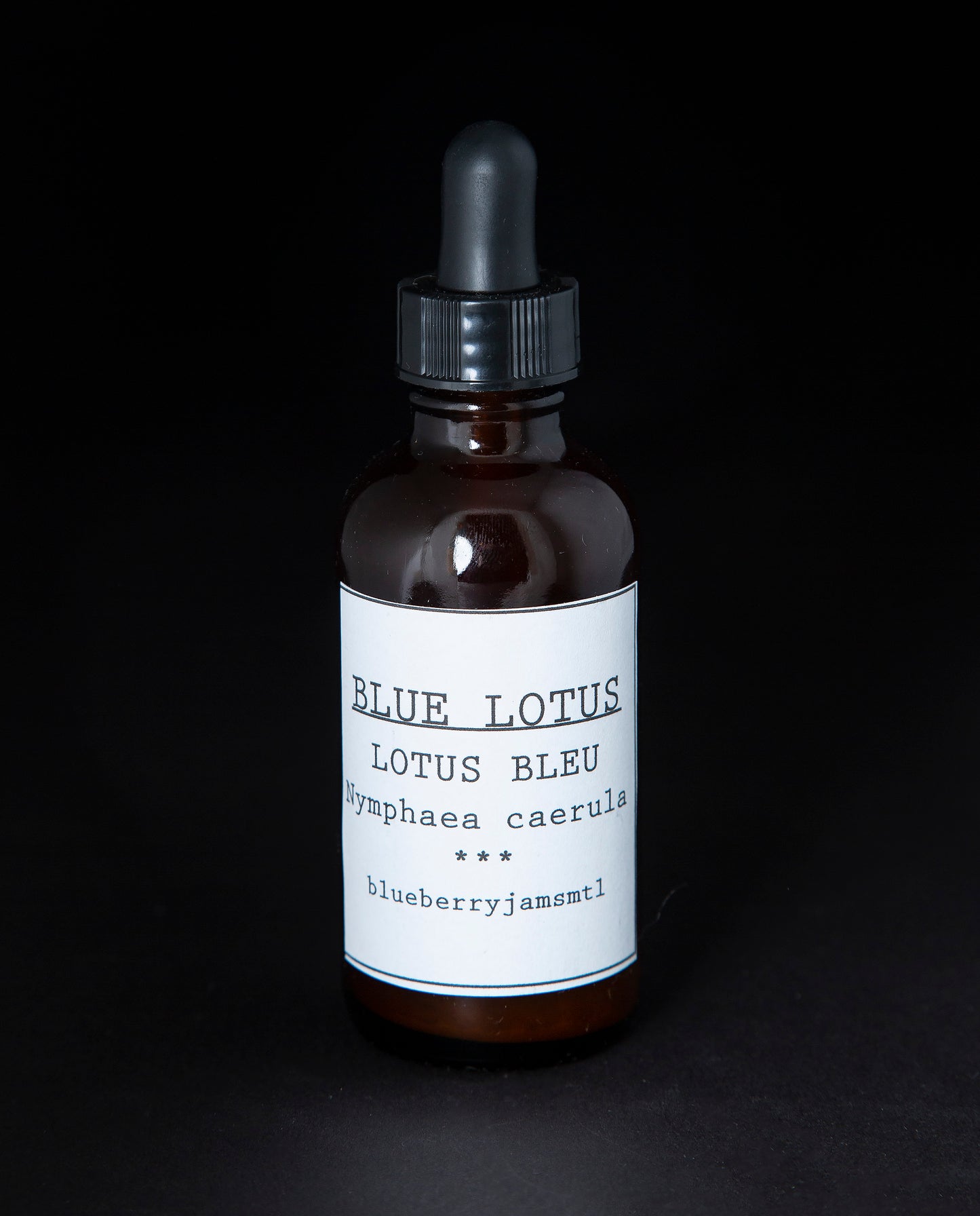 Amber glass bottle with black dropper top containing blueberryjams' blue lotus tincture. The bottle has a white label