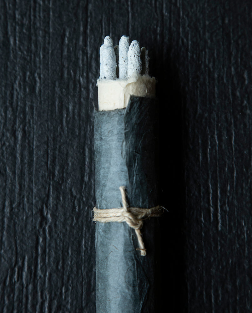 close up of the the tip of a bundle of copal incense sticks wrapped in black natural paper and twine on black wooden background