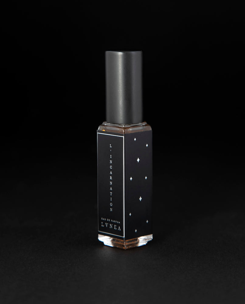 8ml clear bottle of LVNEA'S L'Incarnation natural perfume on black background, bottle is rotated at a 3/4 angle exposing a star pattern on the label.