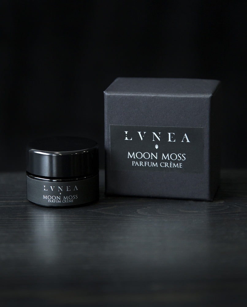 10g black glass jar of LVNEA's 'Moon Moss' vegan solid perfume, sitting next to its black box on a black wooden surface.