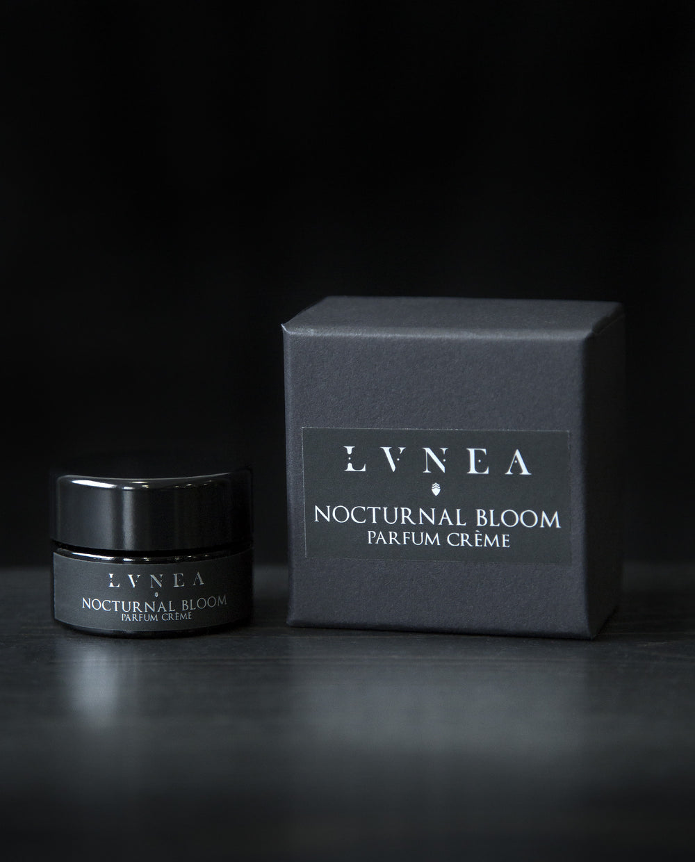 10g black glass pot of LVNEA's Nocturnal Bloom solid perfume next to its box on black background