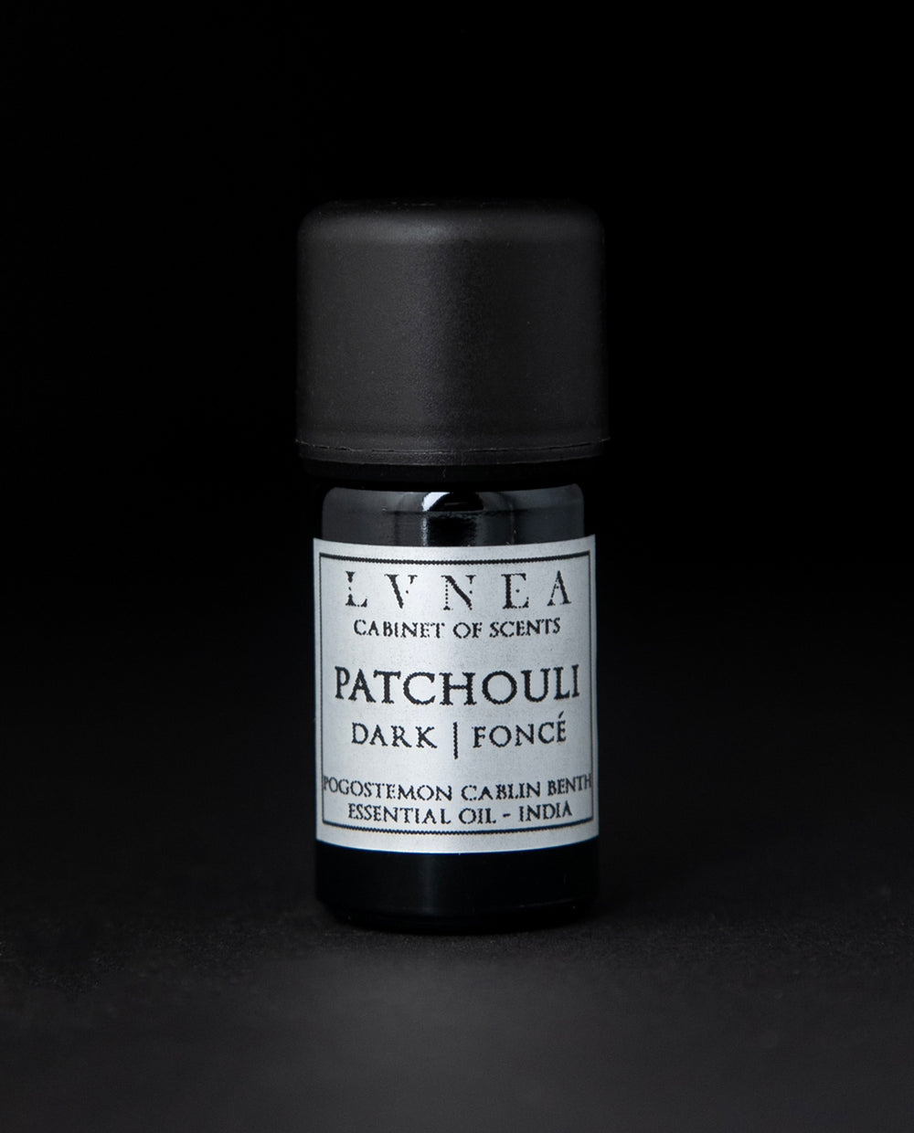 5ml black glass bottle of LVNEA's patchouli essential oil on black background. The label on the bottle is silver.