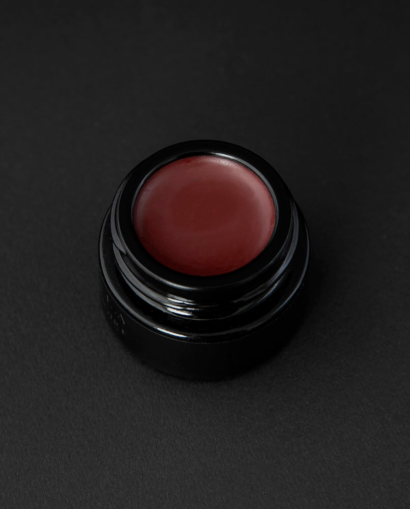 A deep, rosy blush coloured lip balm in a black glass pot on black background